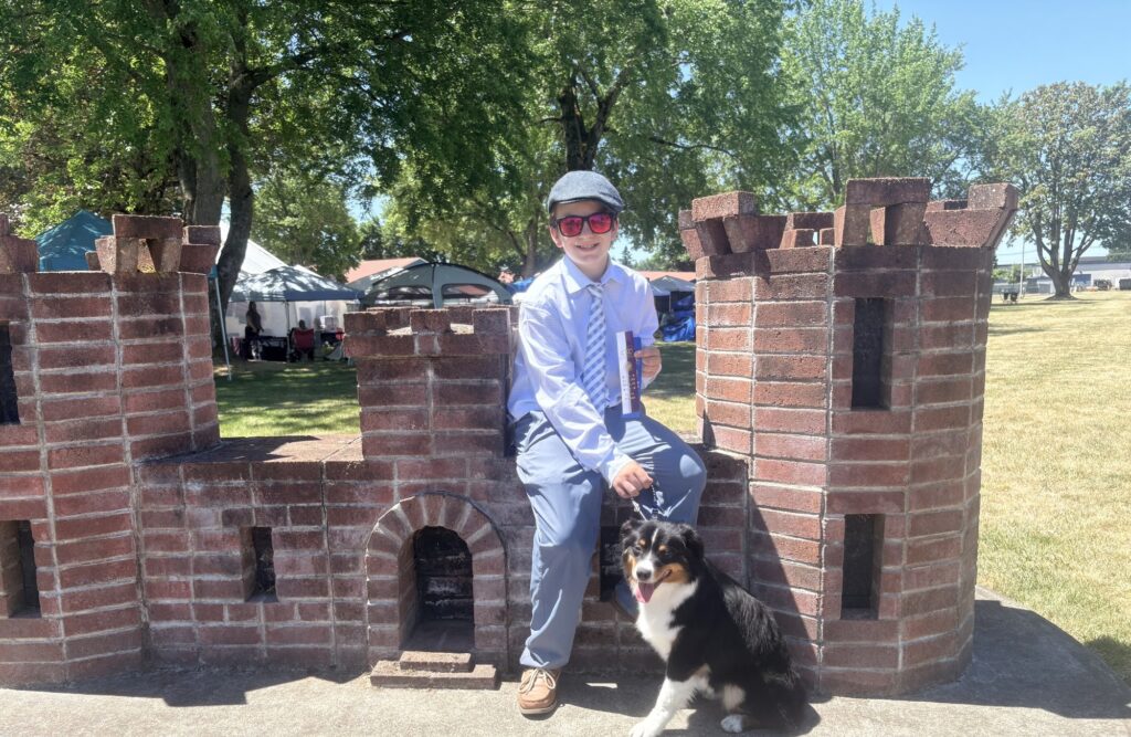 Adrian sitting on a brick castle wall with a ribbon, Emerald at his feet